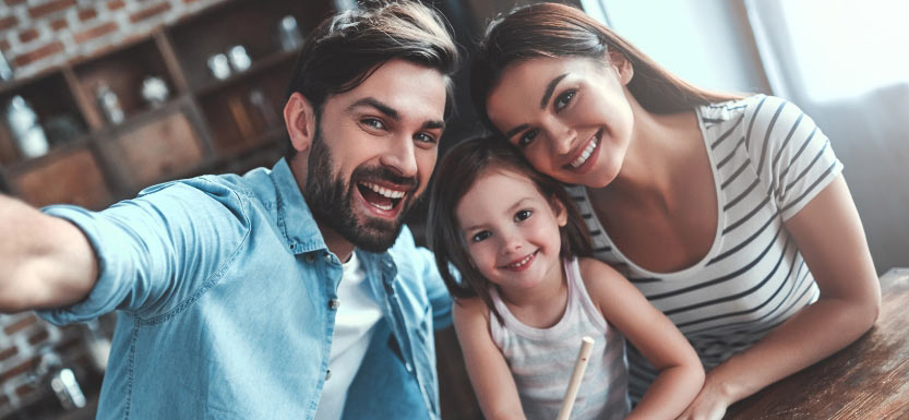Happy family of three smiling together, representing family dental care at a dentist in Langley